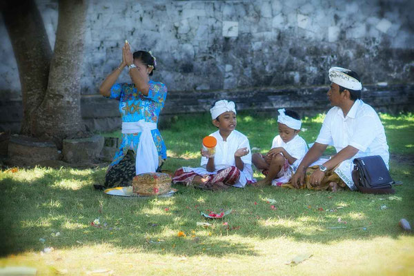 Parents with young children, all in ceremonial attire, taking part in a Balinese ritual.