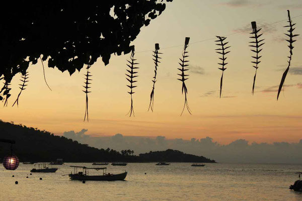 Sunset over the sea with traditional fishing boats silhouetted against the horizon.