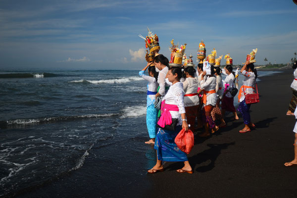 Women carrying offerings toward the ocean in a coastal ritual.