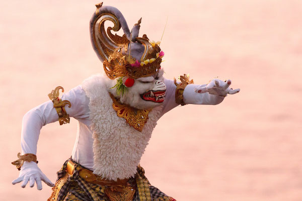 A masked kecak performer captured in a dramatic seaside dance at dusk.