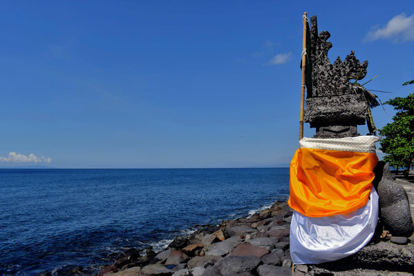 A seaside shrine draped in yellow and white cloth, standing quietly beside the ocean in Jasri Karangasem