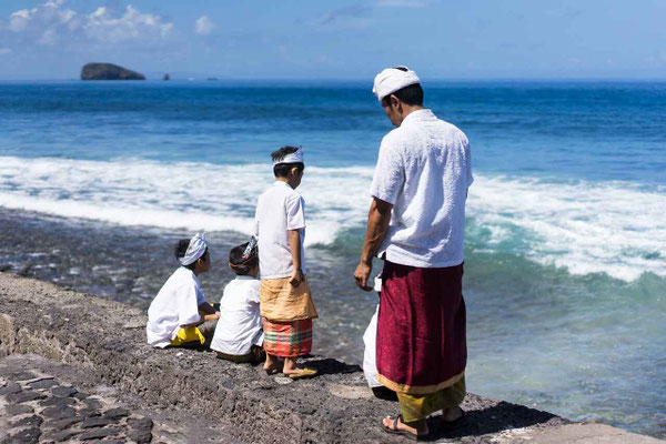 A man with his children performing a coastal ceremony in Candidasa, dressed in traditional Balinese cloths.
