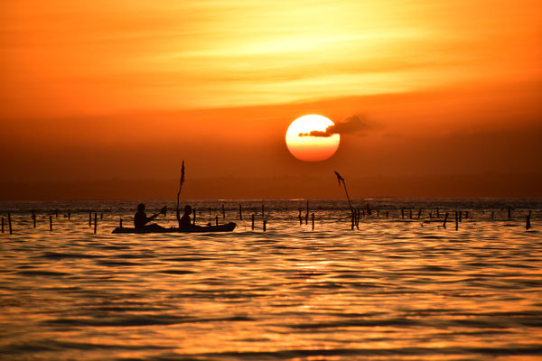 Sunset over Lovina Beach with fishing boats silhouetted at sea.
