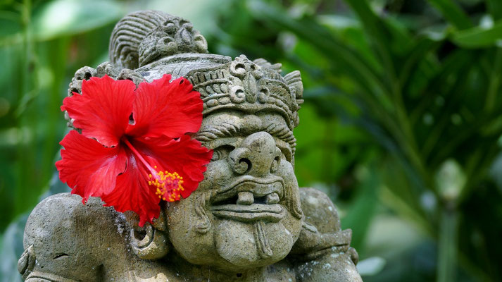 A playful stone guardian adorned with a bright red hibiscus.