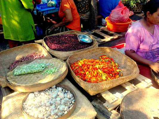 A traditional market stall displaying baskets of chilies, garlic, and beans.