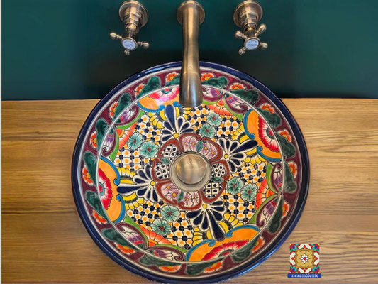 Rundes mexikanisches Waschbecken mit floralem Talavera-Muster in kräftigen Farben – Modell FRIDA – von oben fotografiert, auf Holzplatte mit Wandarmatur, farbenfrohes Design für individuelle Badezimmer.