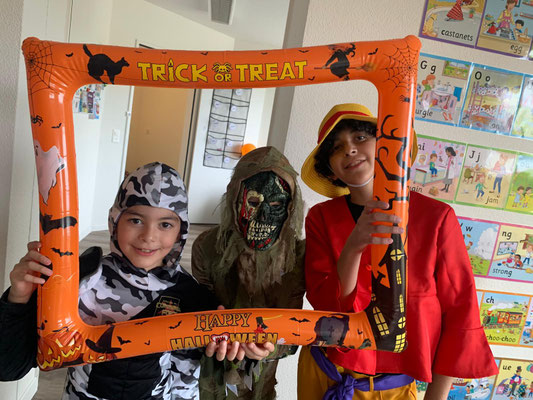 Children posing with a Halloween photo frame during a Custom Kids celebration.