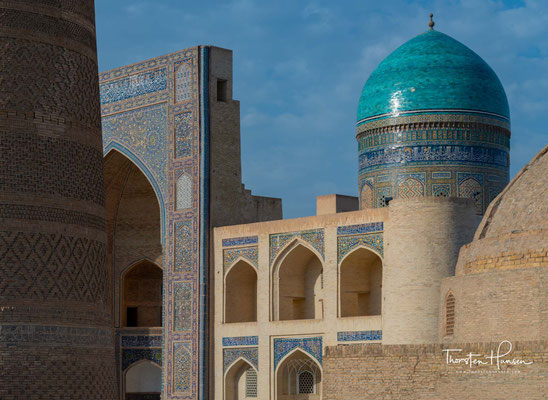 Das Minarett steht an der Südseite des Platzes zwischen der Kalon-Moschee (vollendet 1514) und der Mir-Arab-Madrasa (vollendet 1536/37), die einander im Kosch-Prinzip gegenübergestellt sind. 