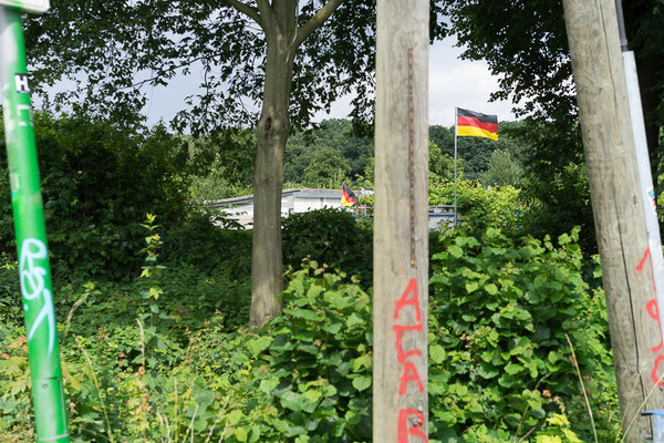 Blick über eine Kleingartenanlage bei Münster-Nord. Im Hintergrund ist eine Deutschlandfahne zu sehen. Im Vordergrund Graffitis: ACAB und 1906