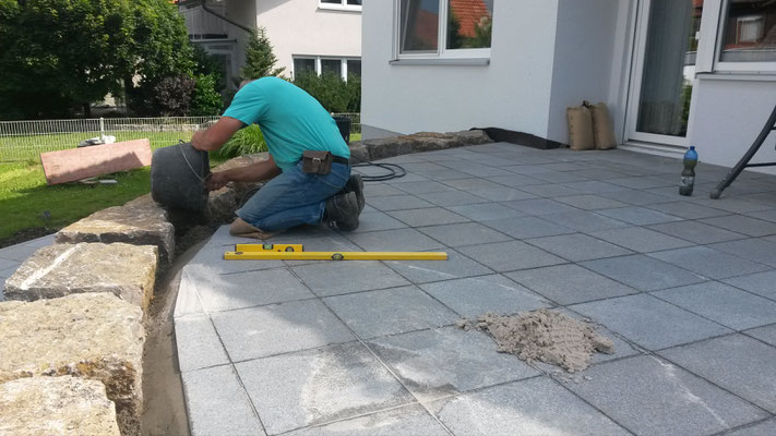 Terrassenplatten wurden verlegt und eingeschnitten. Jetzt werden die äußeren Platten mit einer seitlichen Betonschulter fixiert.