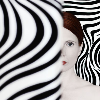 Manuela Deigert Projekte Selbstportrait zur Hälfte verdeckt mit schwarzweißen psychedelisch grafischem Hintergrund
