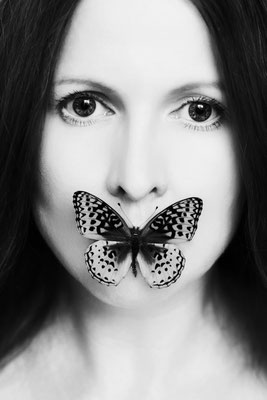 Manuela Deigert Fotokunst Start, Künstlerisches Selbstportrait in schwarz weiß mit einem Schmetterling im Mund