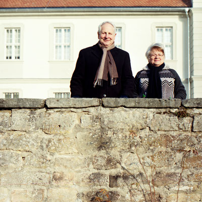Manuela Deigert Mittelformat Ältere Frau mit Mann hinter einer beigen Mauer