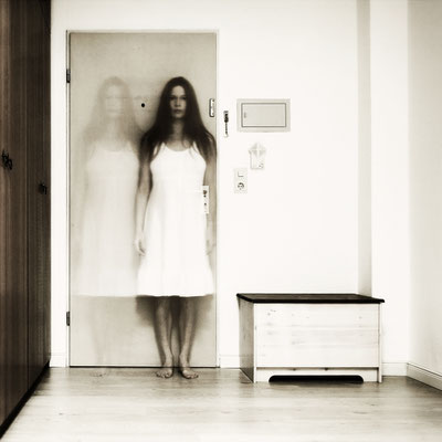 Manuela Deigert Fotokunst Start, Multiple, Langzeitbelichtung eines Selbstportraits in doppelter Ansicht, stehend in einem Raum vor einer Tür, seitlich jeweils eine Holzkiste und Schrank