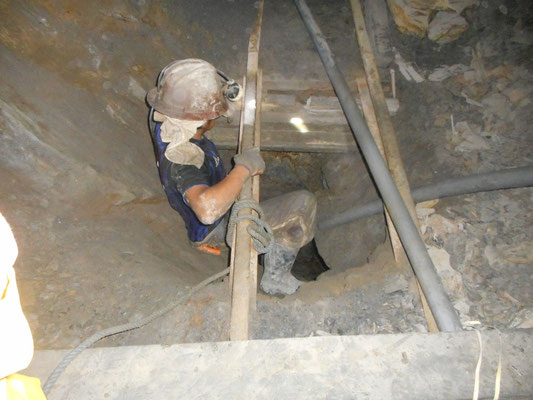 un mineur qui remonte par un trou creusé sous les rails