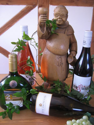 Eine hölzerne Mönchfigur und vier Flaschen Weine und Spirituosen