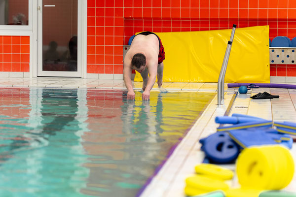 Teilnehmer der inklusiven Schwimmgruppe Belugas übt am Beckenrand den sicheren Einstieg ins Wasser.