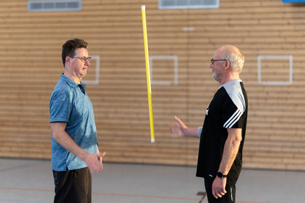 Zwei Teilnehmer des Herz- und Rehasports beim BSV Achim üben Koordination mit einem Trainingsstab in Partnerarbeit.