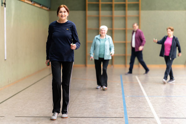 Lungensport beim BSV Achim: Ältere Frau geht lächelnd durch die Turnhalle, im Hintergrund trainiert die Gruppe.