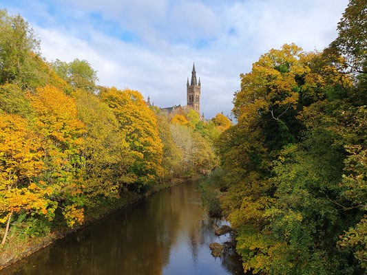 Blick von einer Brücke über den Kelvin River, der gesäumt ist von Bäumen im Herbstlaub, zur alten Universität von Glasgow, Schottland ©My own Travel