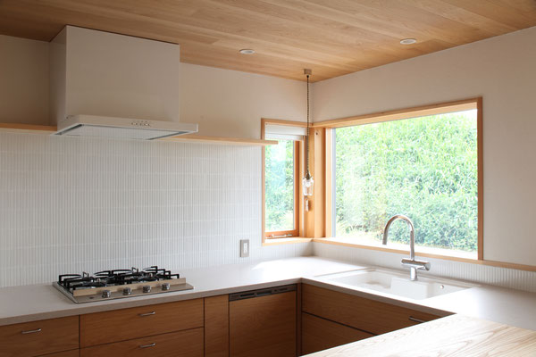 キッチンはL型の人工大理石と手前の木カウンターによるコの字型　天井は板張りにして温かみを出している