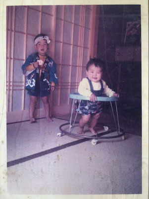 法被を着てお菓子を持つ男の子と、歩行器に乗る笑顔の赤ちゃんの古い家族写真。全体的に色褪せと細かいシミ、画面中央の折れ目が目立つ状態