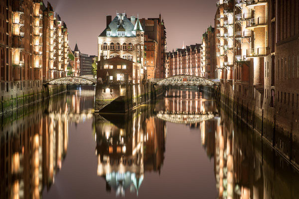 Hamburgs beleuchtete Speicherstadt spiegelt sich nachts im ruhigen Wasser des Fleets