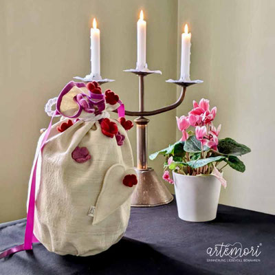 Urne aus Wildseide mit Filzblumen auf einem Altar mit einem dreiarmigen Kerzenleuchter und Alpenfeilchen