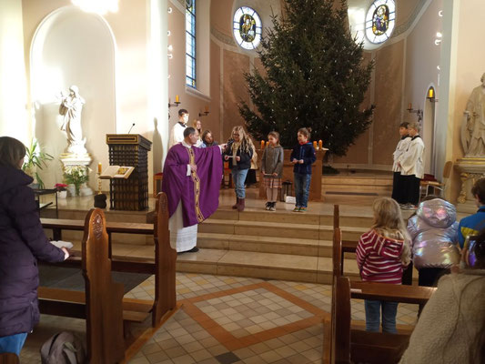 Pfarrer Schmitz hält vier angehenden Erstkommunionkindern auf den Treppenstufen zum Altar das Mikrofon hin, in das sie ihre Fürbitten sprechen