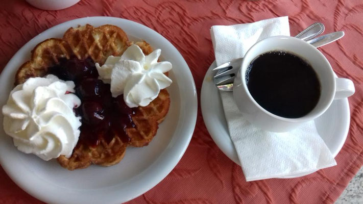 Eine gute Tasse Kaffee und eine Waffel mit Kirschen und Sahne