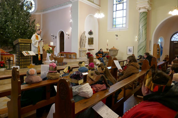Wir sehen in Kirchenbänken sitzende Sterninsger, denen Pfarrer Schmitz, auf den Stufen des Altarraums stehend, die Aktion erläutert.