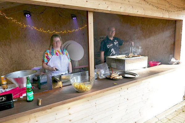 Grillmeister und Grillmeisterin stehen in der Bude hinter Grill und Friteuse