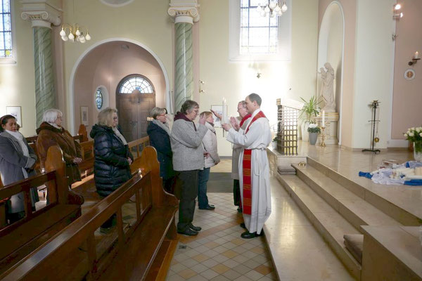 Pfarrer Schmitz und Diakon Becker stehen am Fuß des Altarraums und spenden hier mit gekreuzten Kerzen den Blasiussegen.