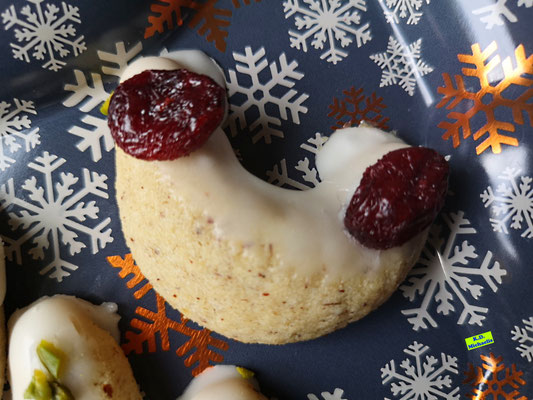 Nahaufnahme eines Zitronen-Haselnuss-Kipferls mit getrockneten Cranberrys/Cranberries nach einem Backrezept aus eBook/Backbuch Dinkel-Weihnachtsplätzchen von K.D. Michaelis