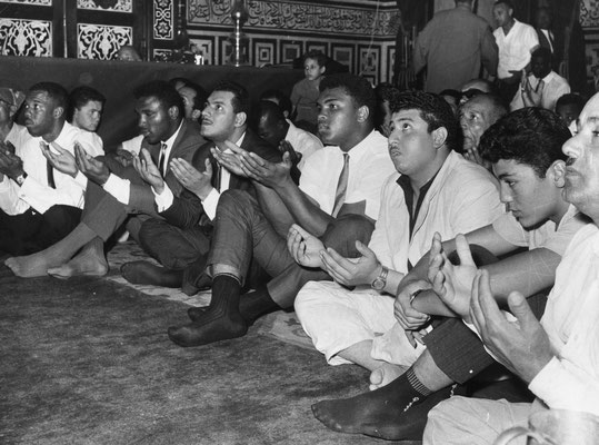 American boxer Muhammad Ali (4th from Right) prays with his hands open in a crowd at the Hussein Mosque in Cairo, 1964, Egypt (GettyImages/Express)