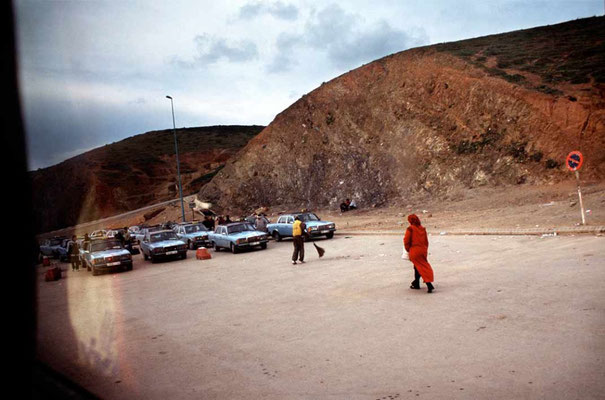 An arabian woman walks towards some cabs waiting for possible customers in the desert land over the border. The bus carries on its travel. The next stop is Casablanca.