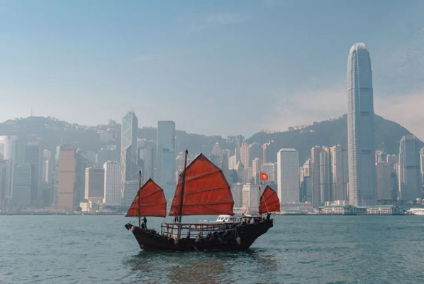Das Bild zeigt den Victoria Harbour in Hongkong mit einer traditionellen Dschunke vor der Skyline