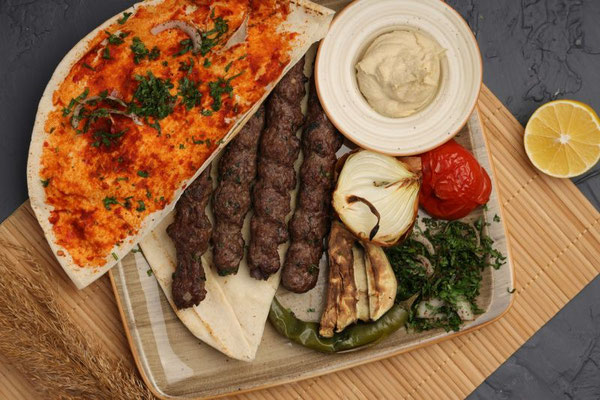 Eine mediterrane Platte mit Adana Kebab-Spießen, gegrillte Zwiebel, Tomate und Paprika