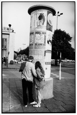 Ein Paar steht an der Litfasssäule vor dem Kino International in der Karl-Marx-Allee. Im linken Bildrand sieht man Mokka-Milch-Eisbar. Aufgenommen 1985.