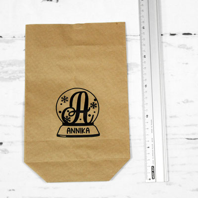 Braune Papiertüte mit “Annika” und einem Monogramm, neben einem Lineal auf Holzuntergrund.