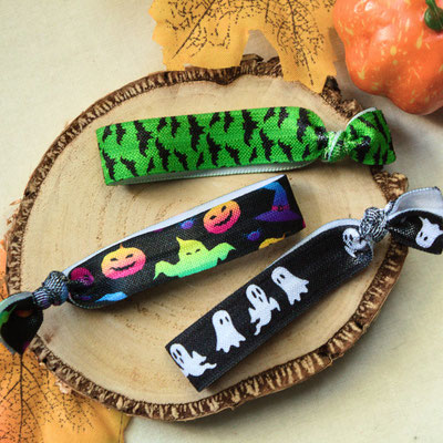 Drei Armbänder mit Halloween-Motiven auf einer Holzscheibe, umgeben von Herbstlaub.
