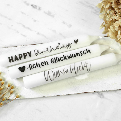 Drei weiße Stabkerzen mit ‘HAPPY Birthday, Herzlichen Glückwunsch, Wunschlicht’ und Trockenblumen.