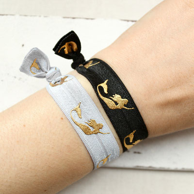 Zwei Armbänder mit Meerjungfrauen-Motiven, eines schwarz und eines weiß, werden am Handgelenk getragen.