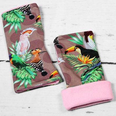 Zwei Armstulpen mit tropischen Vogelmotiven, darunter Tukan, Kakadu und andere Vögel, auf einem weißen Holzhintergrund.
