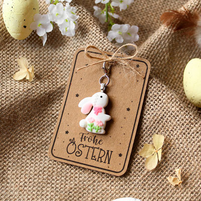 Frohe-Ostern-Karte mit Hasenschlüsselanhänger auf Jute, umgeben von Blumen und gelben Eiern.