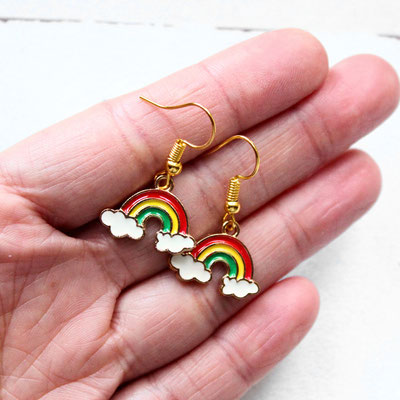 Hand hält Regenbogen-Ohrringe mit Wolken, goldene Haken, weißer Hintergrund.