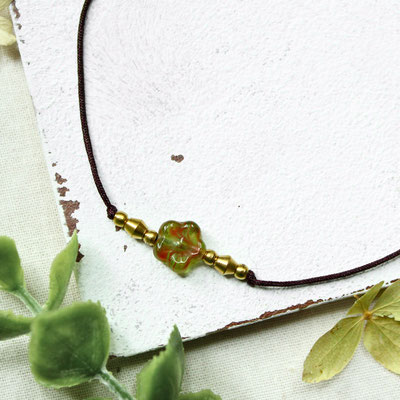 Fußband mit grüner Blumenperle und goldenen Perlen auf weißem Untergrund.