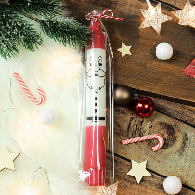Eine in Plastik verpackte, weihnachtliche Stabkerze mit einem Weihnachtsmann-Gesicht, umgeben von Weihnachtsdekorationen wie Zuckerstangen und Sternen.