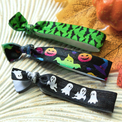Drei Halloween-Armbänder mit Spinnen-, Kürbis- und Geistermotiven auf gemusterter Unterlage.