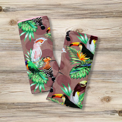 Zwei bunte Armstulpen mit tropischen Vogelmotiven, darunter Tukan, Kakadu und andere, auf einem Holzhintergrund.